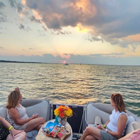 Four women on a boat watching sunset over the ocean.