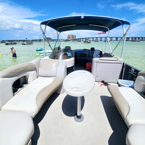 Interior of a boat with canopy, lounging seats, and people swimming nearby in clear water.