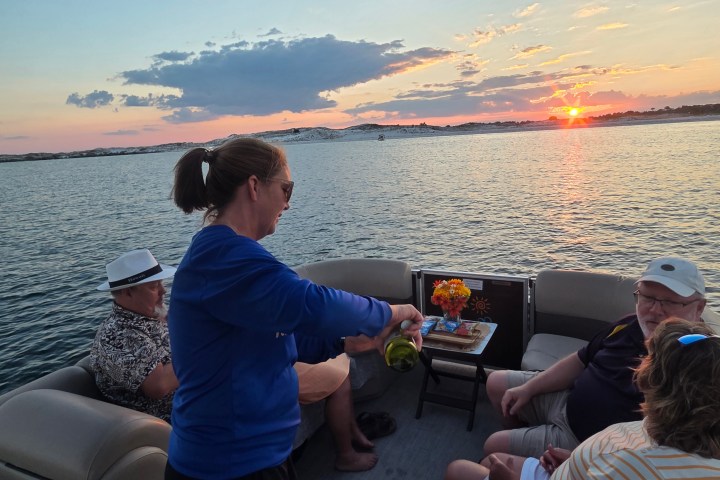 People relaxing on a boat at sunset, with one person pouring a drink.