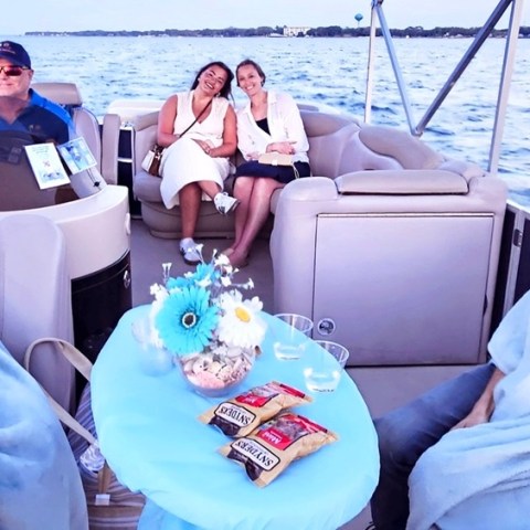 Three couples relaxing under blankets on a boat with snacks on a table.