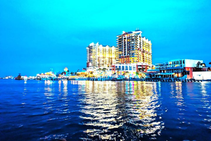 Bright waterfront cityscape with lit buildings reflecting on calm water.