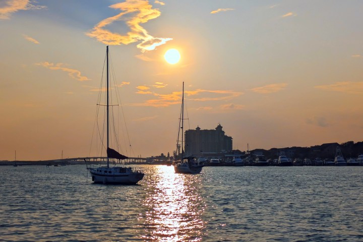 Sailboats on water with sunset and distant buildings.