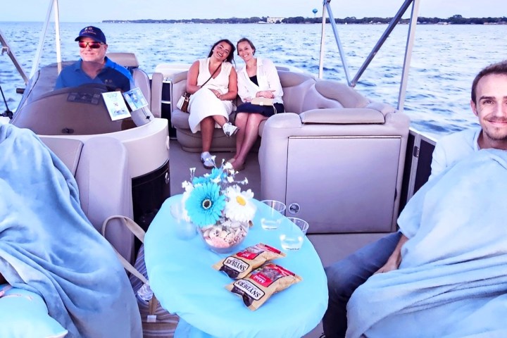 People on a boat, smiling, with blankets and snacks, on a lake.