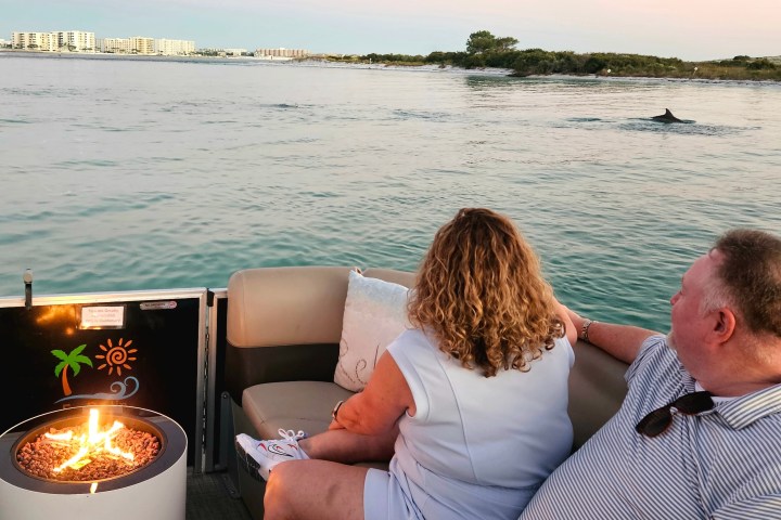 Couple on a boat enjoying a fire pit with a dolphin fin in the water.