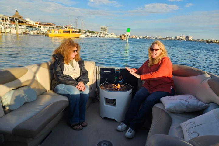 Two people sitting on a boat with a central fire pit on a sunny day.