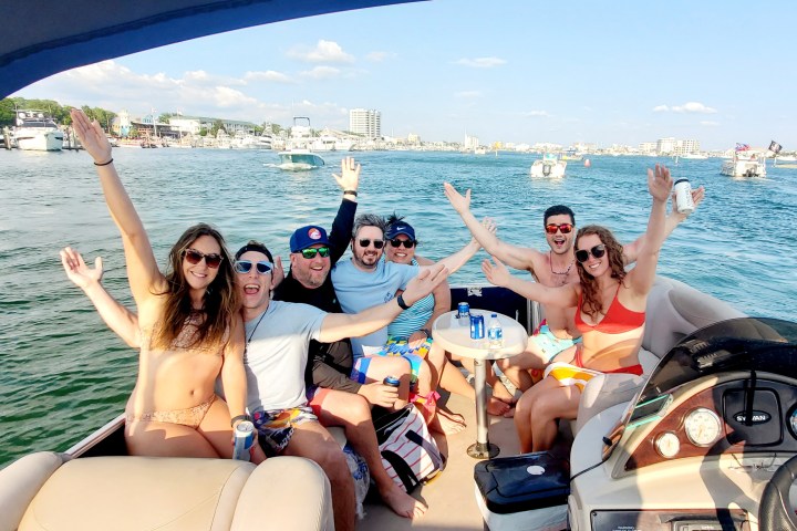 Group of friends enjoying a boat ride, smiling and raising hands.
