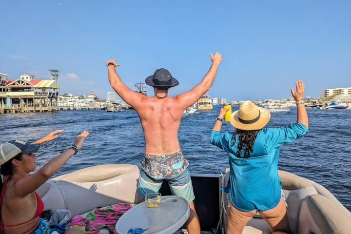 People on a boat, two standing with arms raised, enjoying a sunny day on the water.