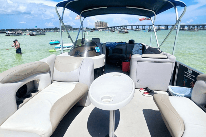 Inside of a yacht with beige seating, view of sandy shore and blue sky in the background.