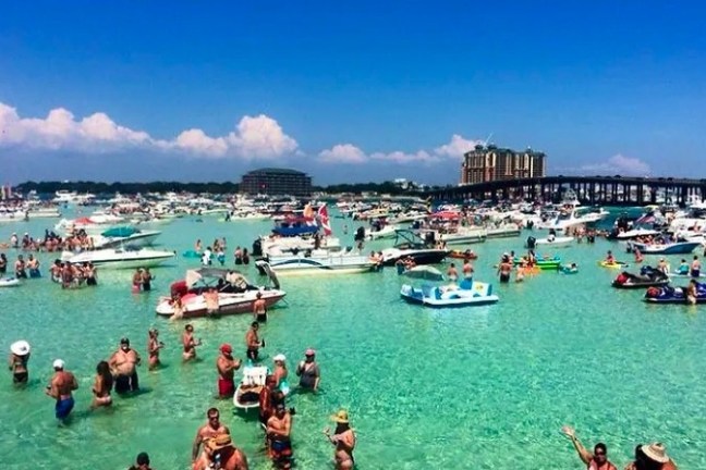 Crowded beach with people swimming and many boats in clear water.