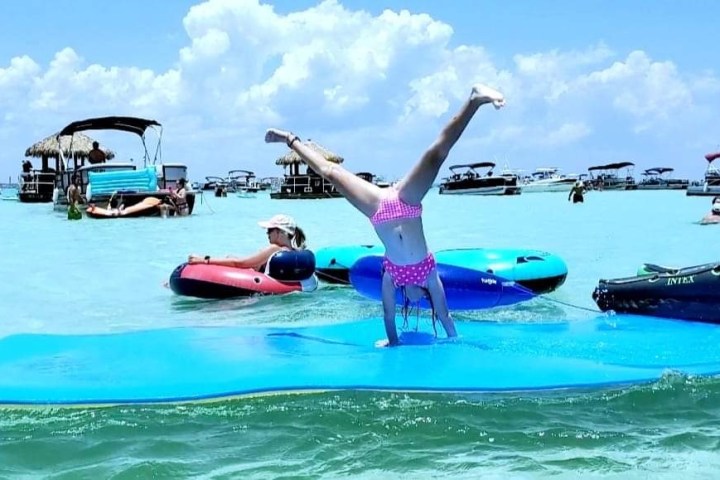 Person doing a handstand on a floating mat in a busy lake.