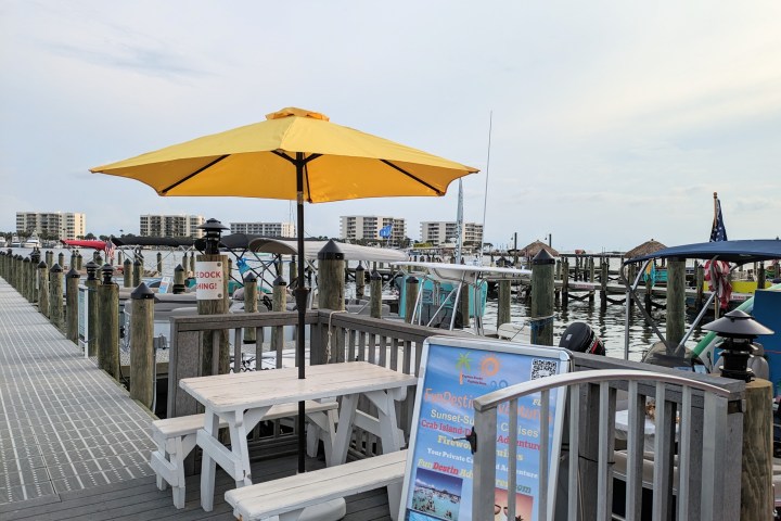 Dockside picnic table with yellow umbrella, boats, and distant buildings.