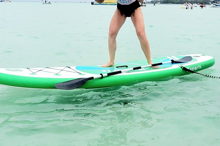 Person on paddleboard in a swimsuit and hat poses playfully on the water.