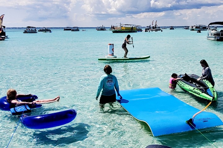 People enjoying water activities with floaties and paddleboards on clear blue sea.