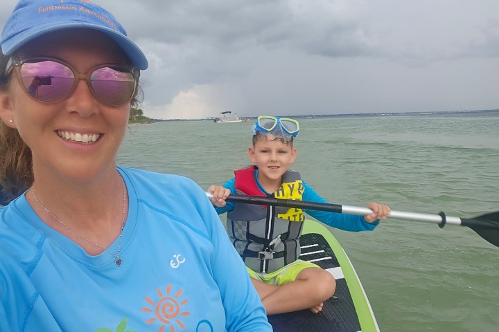 Woman and boy kayaking on calm water, cloudy sky.