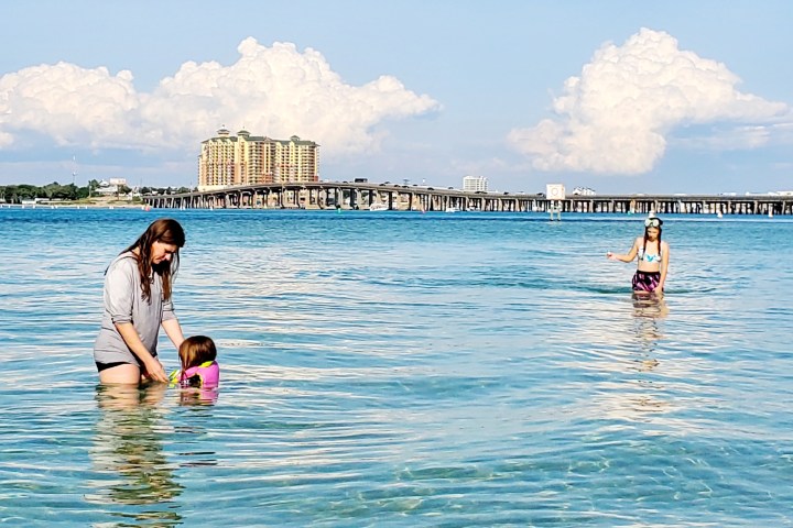 Adults and a child standing in shallow sea water on a sunny day.
