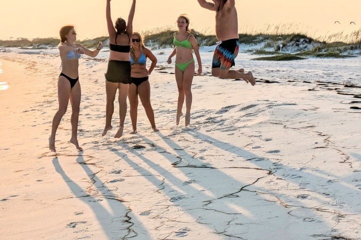 Group of people in swimwear jumping and cheering on a sunny beach.