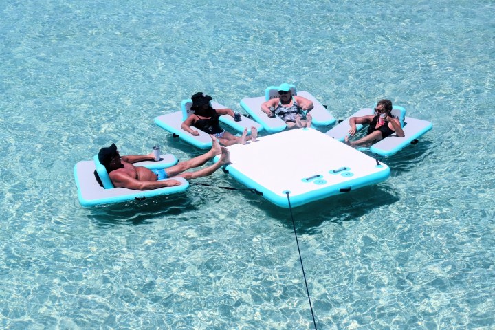 Four people relaxing on floating loungers in clear blue water.