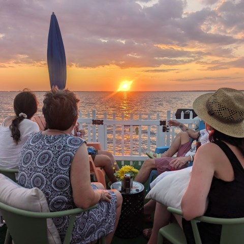 People seated on a boat watching a sunset over the ocean.