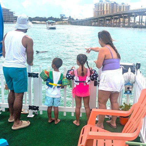 Family of four in swimsuits watching the water from a boat deck.