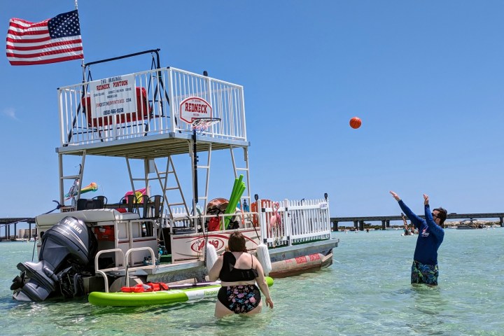 People enjoying a floating boat with an American flag in shallow water under clear blue sky.