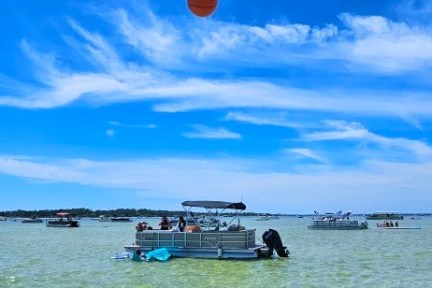 Person in water shoots basketball towards hoop with boats in the background.