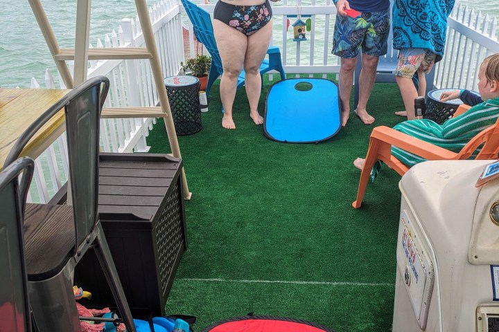 People playing cornhole on a boat deck by the water.