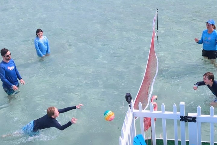 Group of people playing water volleyball near a net in shallow water.