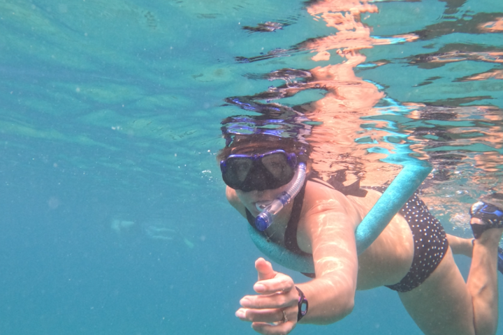 Person snorkeling in clear blue water with a snorkel and mask.