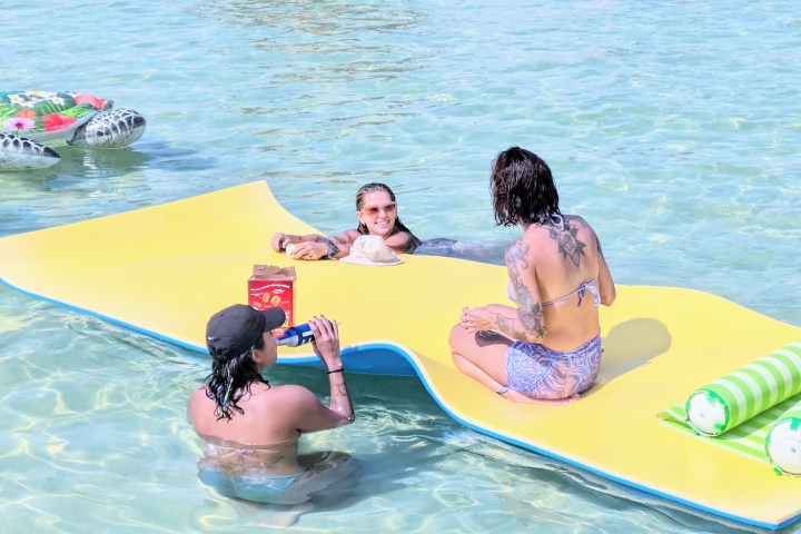 People enjoying a sunny day on a floating mat in the water.