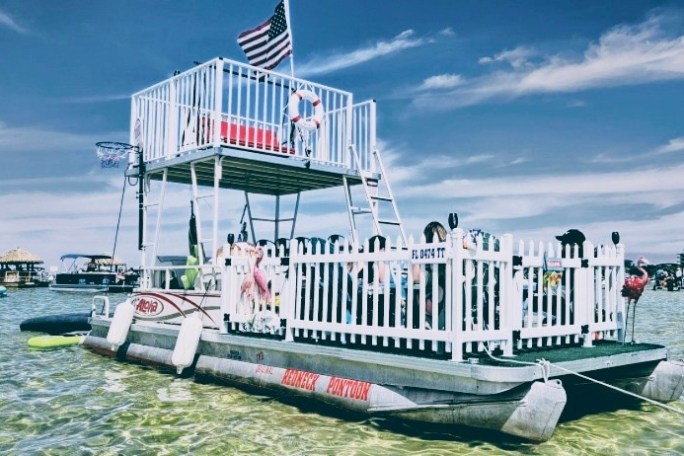 Double-deck pontoon boat with American flag and people relaxing.