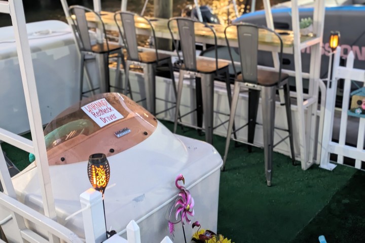 Outdoor bar setting with stools, a boat part, flamingo decor, and yellow flowers.