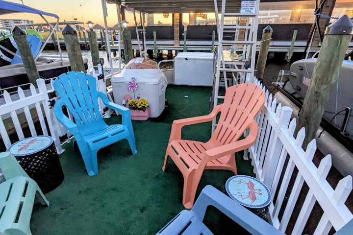 Colorful chairs on a dock with life ring and boats in the background at sunset.