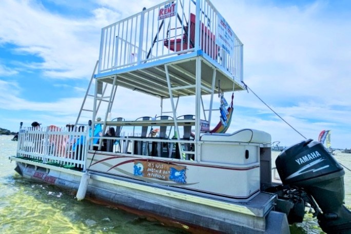 Double-deck pontoon boat with motors, floating on calm water.