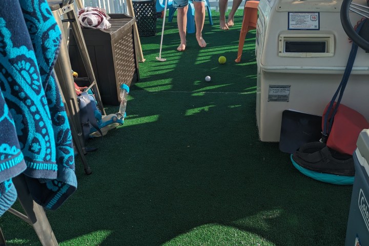 Two kids playing mini golf on a boat deck with green carpet.