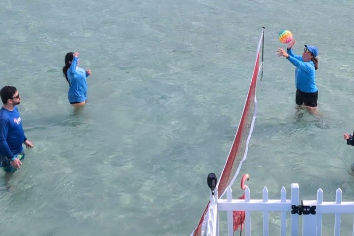 Four people playing water volleyball in a shallow sea near a white fence.
