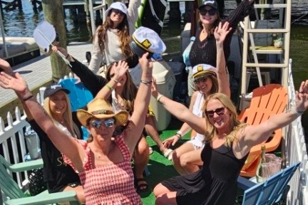 Group of six people posing cheerfully in a fenced area with nautical decor.
