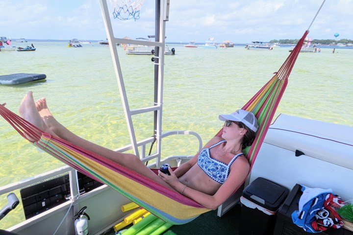 Woman relaxing in a hammock on a boat, surrounded by water and distant boats.