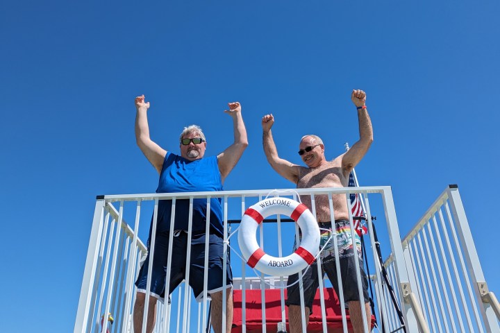 Two men celebrating on a deck with a lifebuoy and clear blue sky.