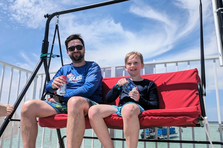 Two people relaxing on a red swing with a bright sky background.