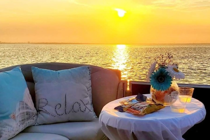 Sunset over water with a cozy sofa, table, snacks, and drinks.
