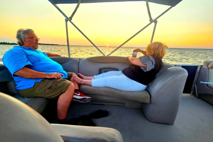 Two people relaxing on a boat at sunset, with water in the background.