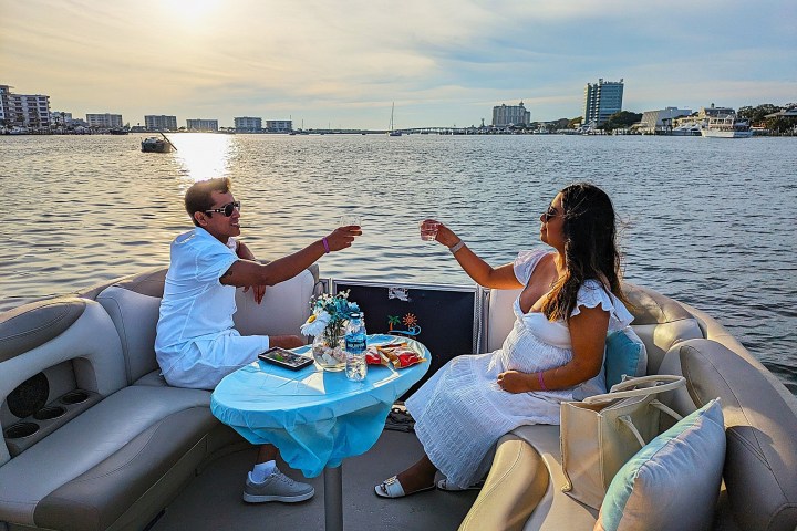Couple toasting on a boat at sunset with cityscape in background.