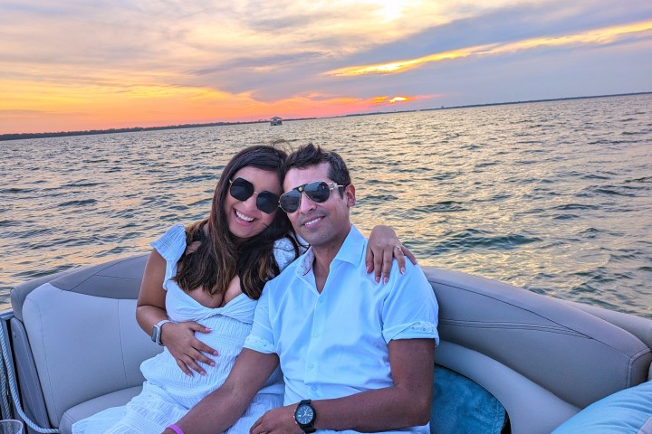 Couple in white clothing sitting on a boat at sunset over a calm lake.