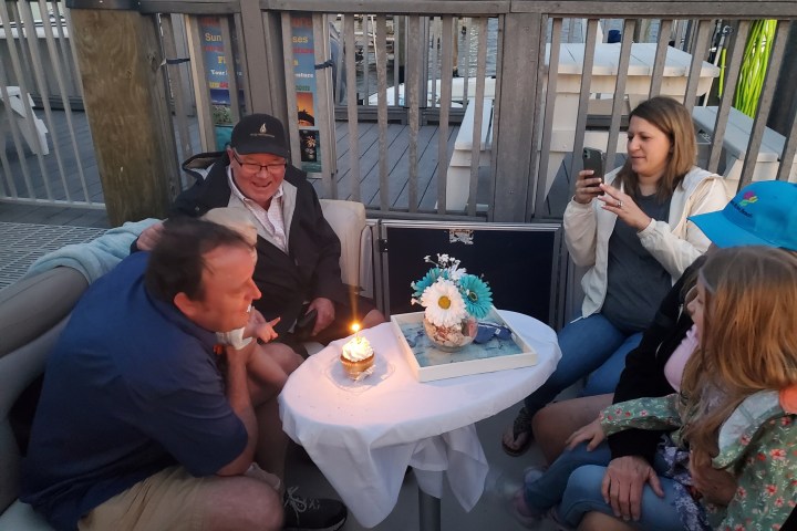 Group of people celebrating with cake and candles on a deck.