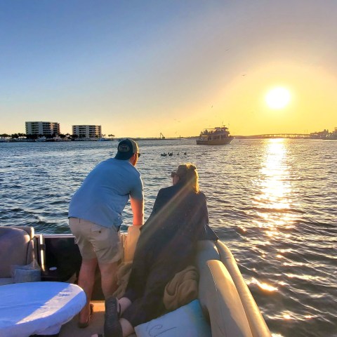 People on a boat at sunset with buildings and calm water.