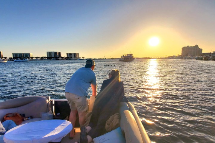 People on a boat at sunset with buildings and calm water.