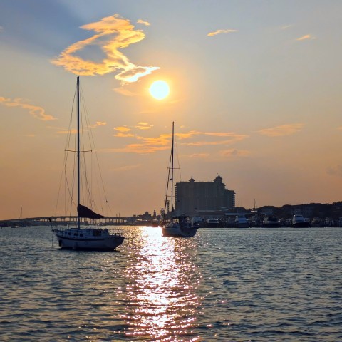 Sailboats on water at sunset with buildings silhouetted on horizon.