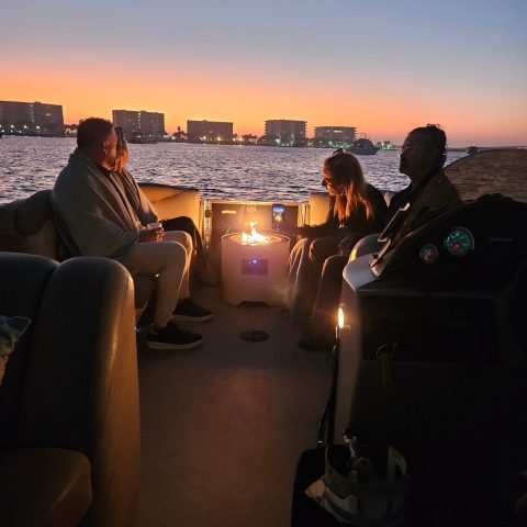 People on a boat at sunset, city skyline in the background.