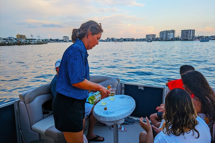 Person pouring drinks for people on a boat with a cityscape in the background.