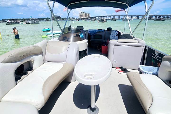 Empty pontoon boat with canopy on clear water, people in background.
